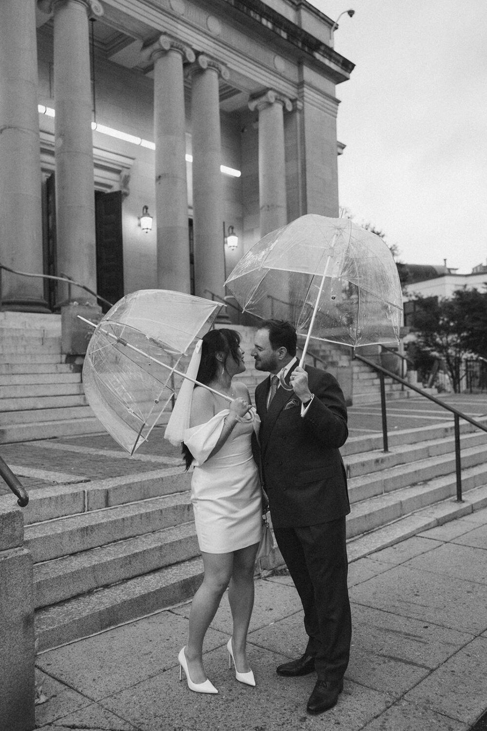 couple poses with clear umbrellas outside of the buildings in Washington DC