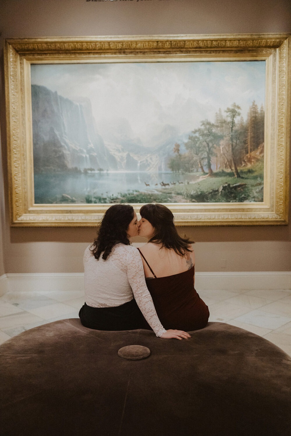 couple kiss in front of large landscape painting