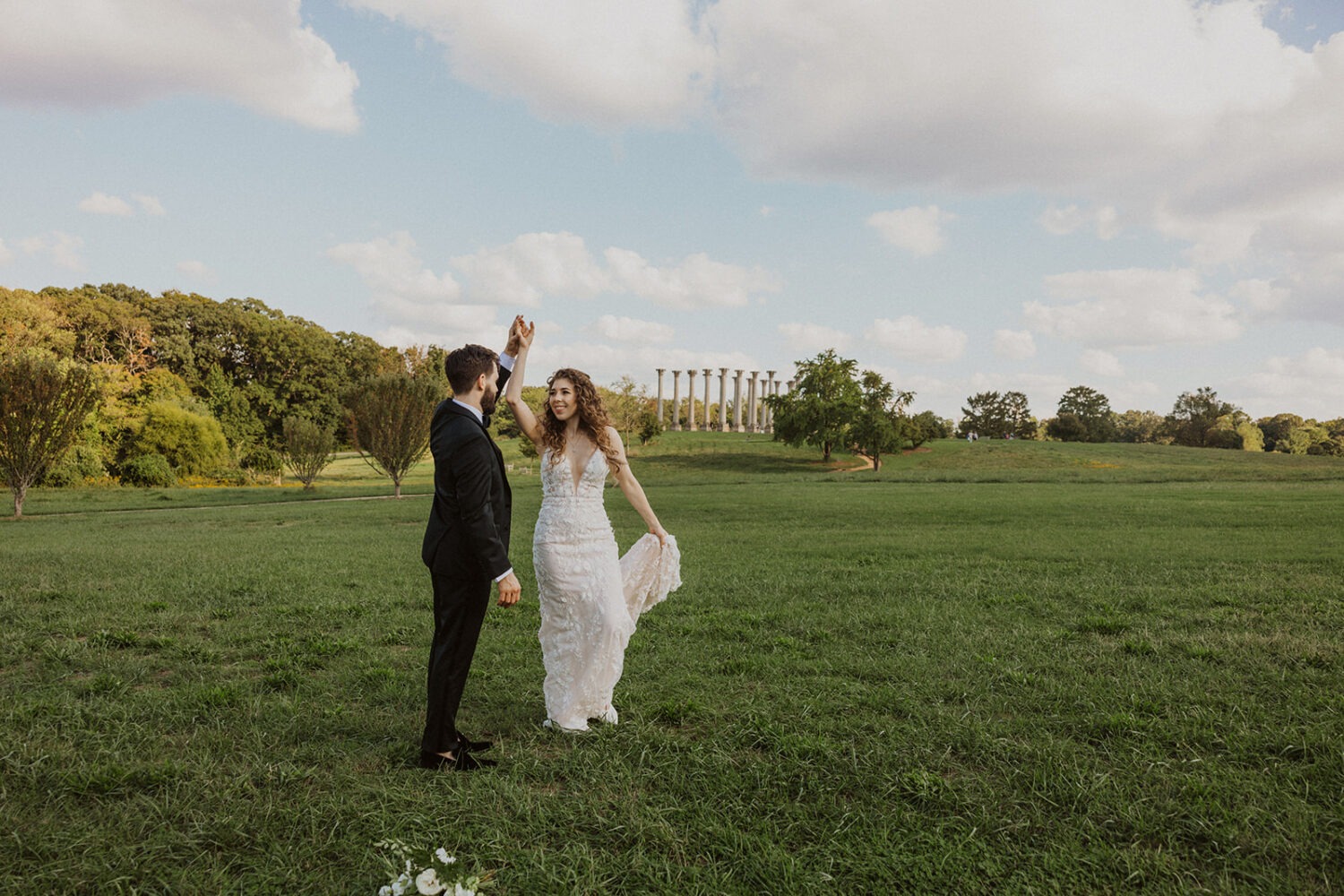 couple poses in Ellipse Meadow with  the National Capitol Columns in the background