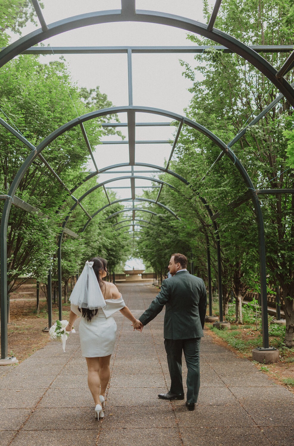 couple hold hands walking under archway of Meridian Hill Park