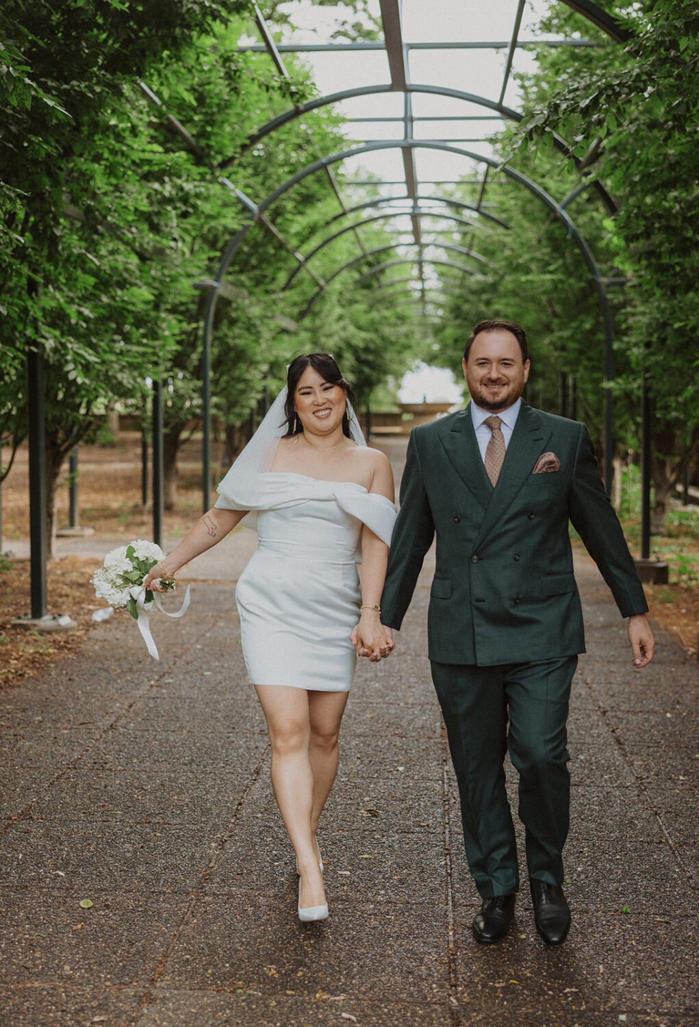 couple hold hands walking under archway of Meridian Hill Park