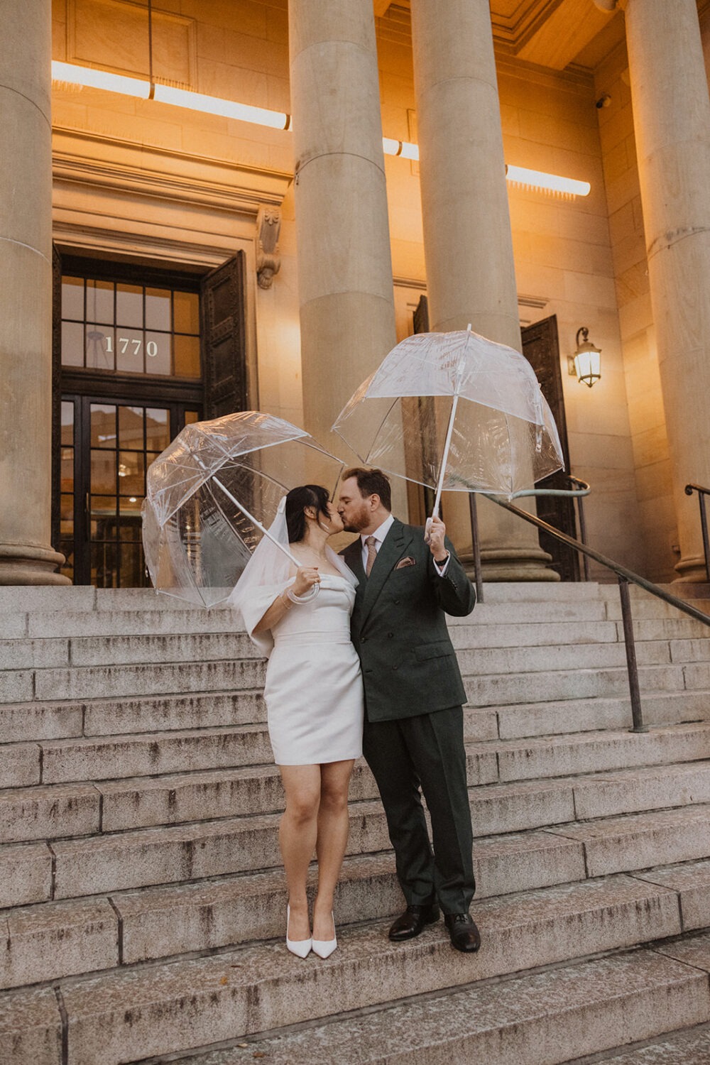 couple kiss on steps with clear umbrellas