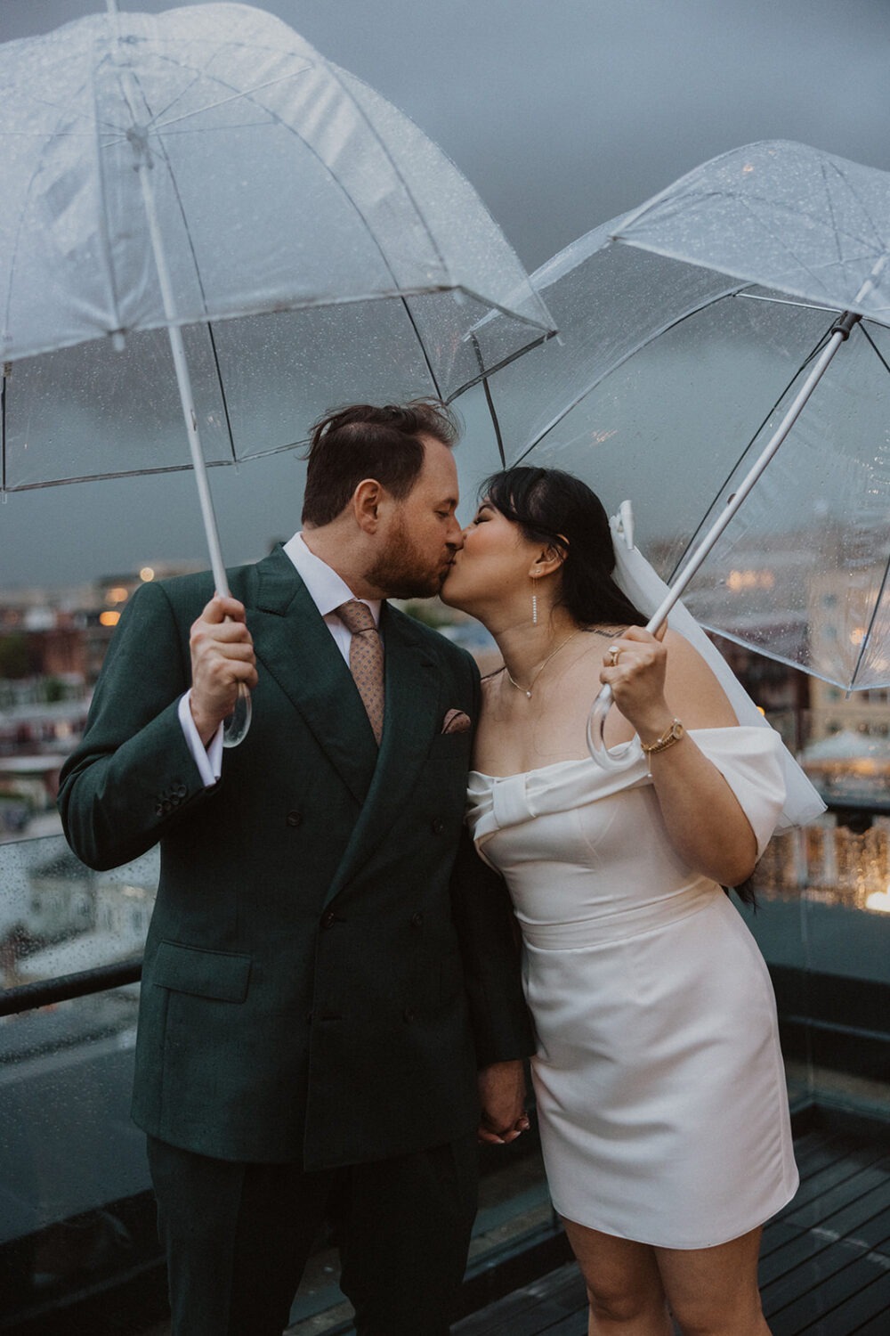 couple kiss with clear umbrellas during rainy wedding day