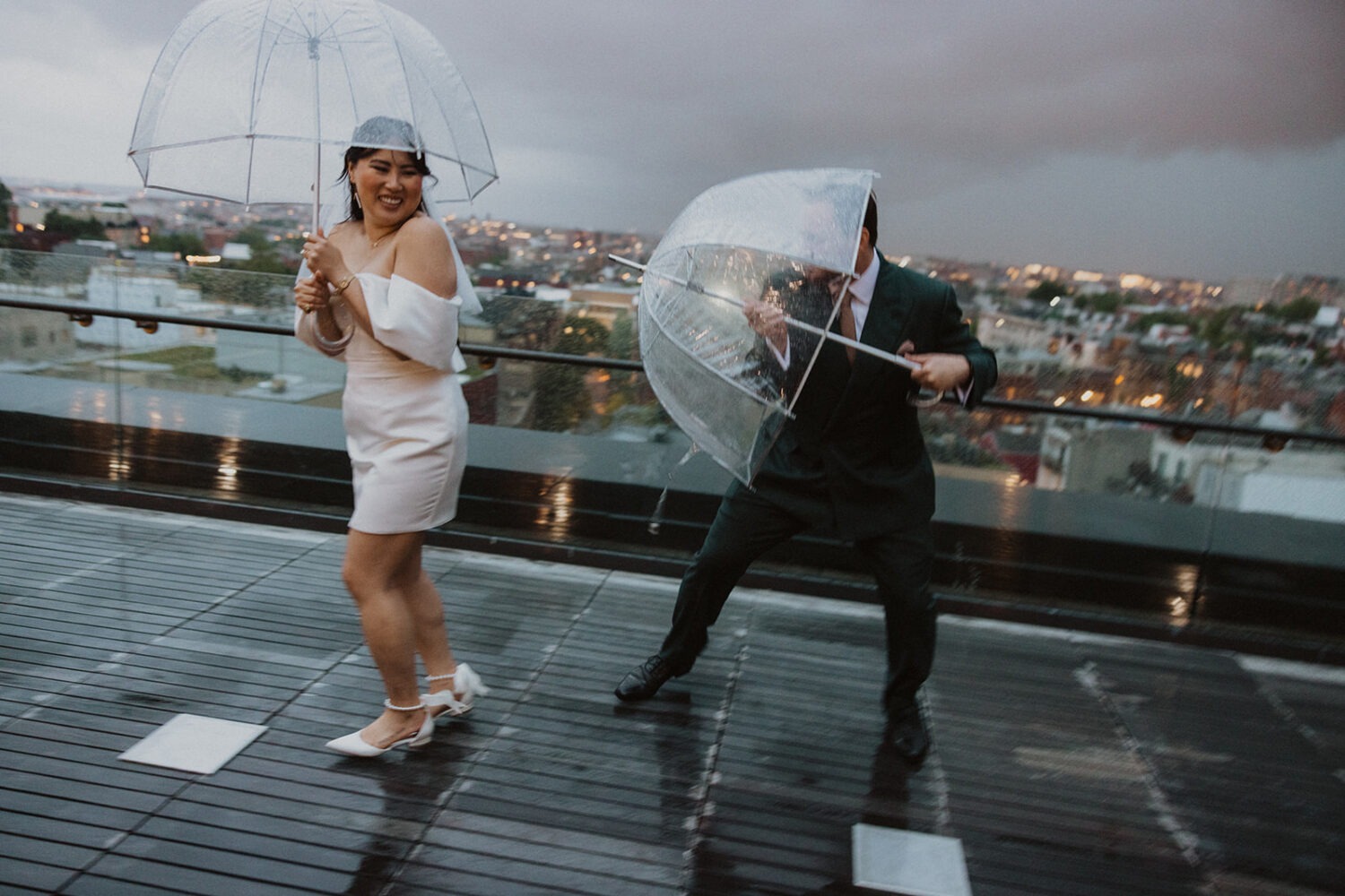 couple plays together with umbrellas during rainy wedding day