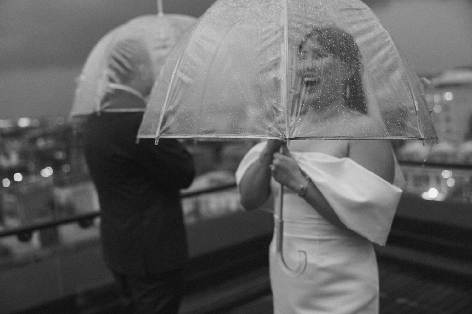 couple plays together with umbrellas during rainy wedding day