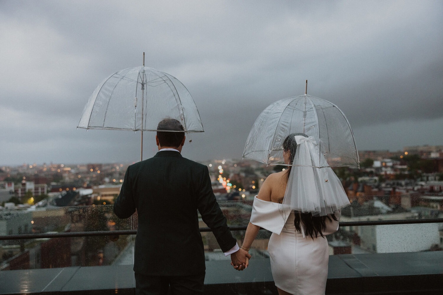 couple holds hands and umbrellas during rainy wedding day
