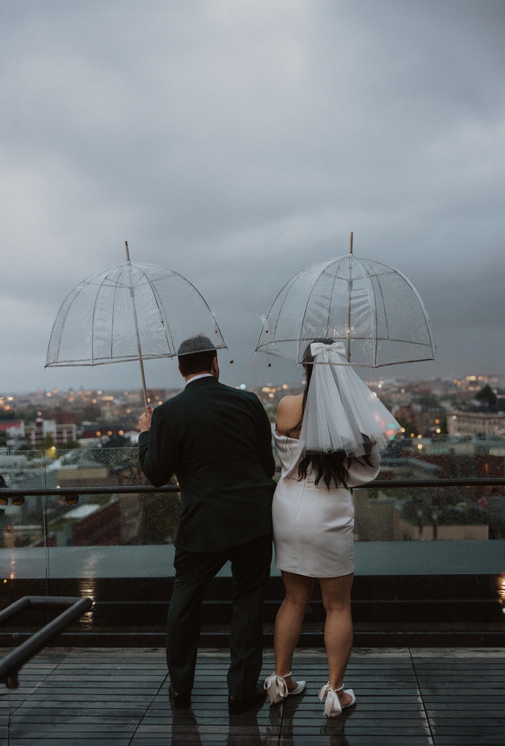 couple plays together with umbrellas during rainy wedding day