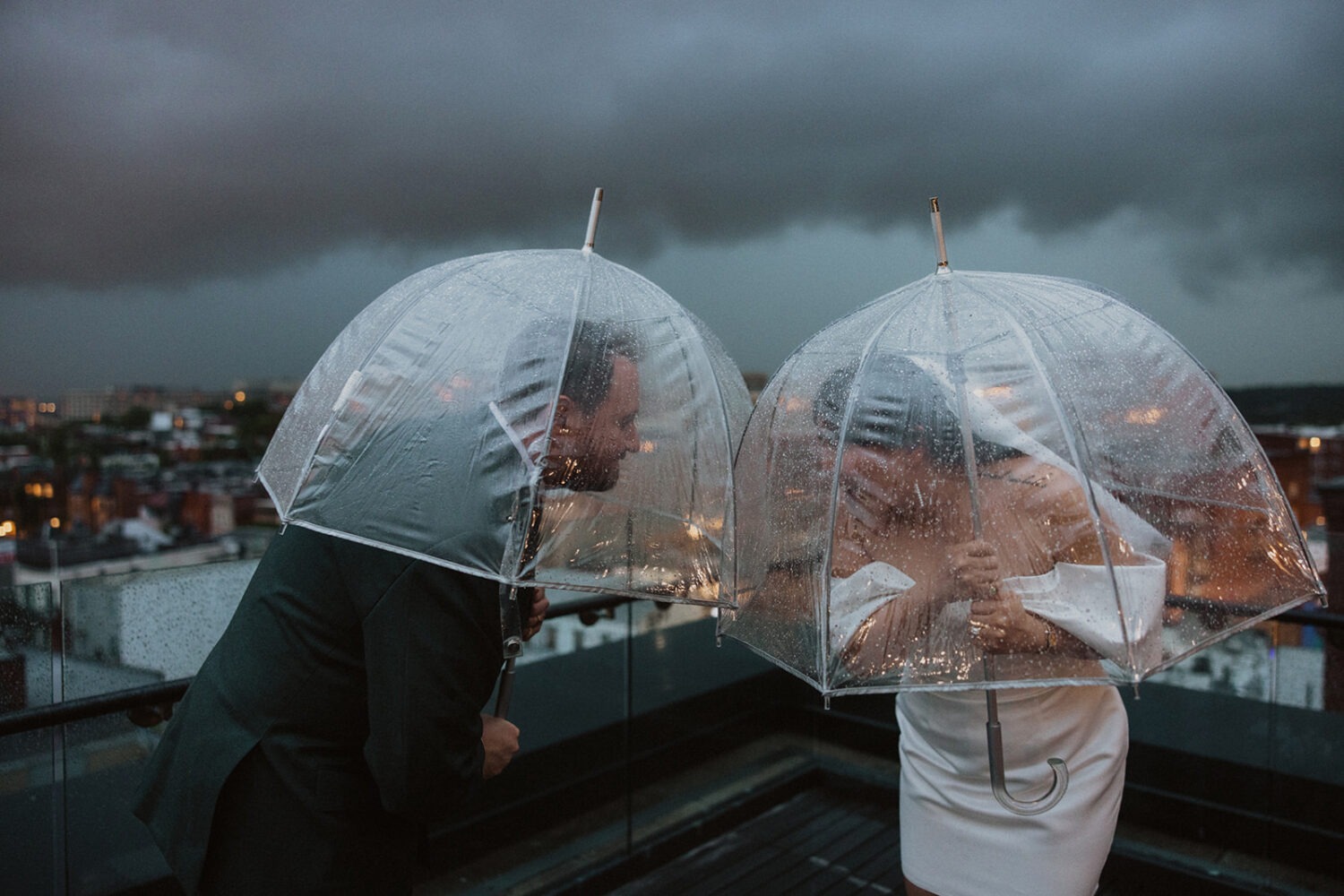 couple plays together with umbrellas during rainy wedding day