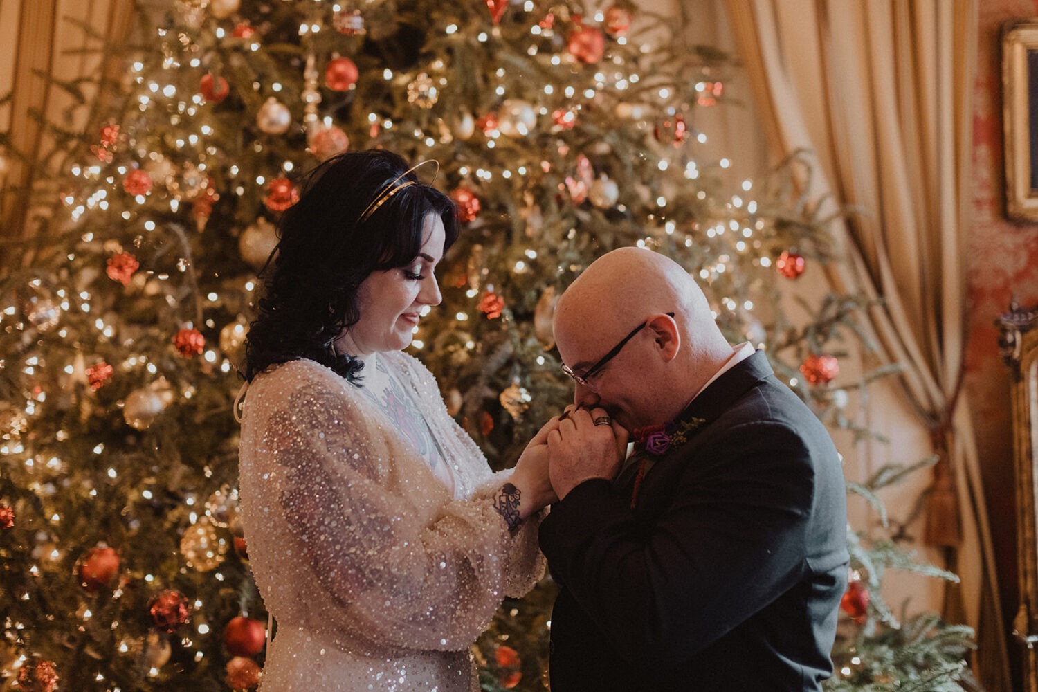couple hold hands while posing in front of Christmas tree