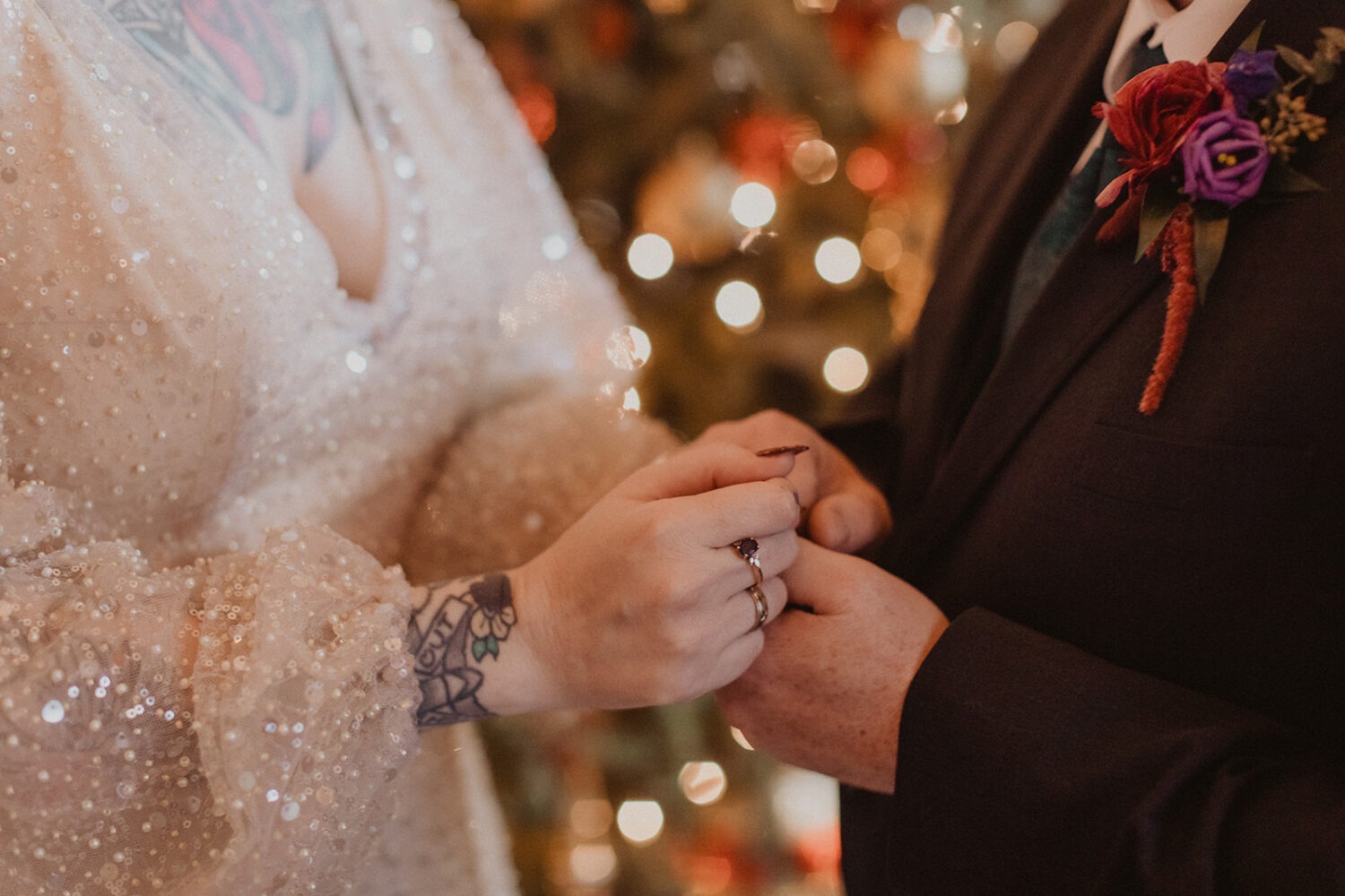 couple holding hands while showing off rings and sparkles from dress and lights