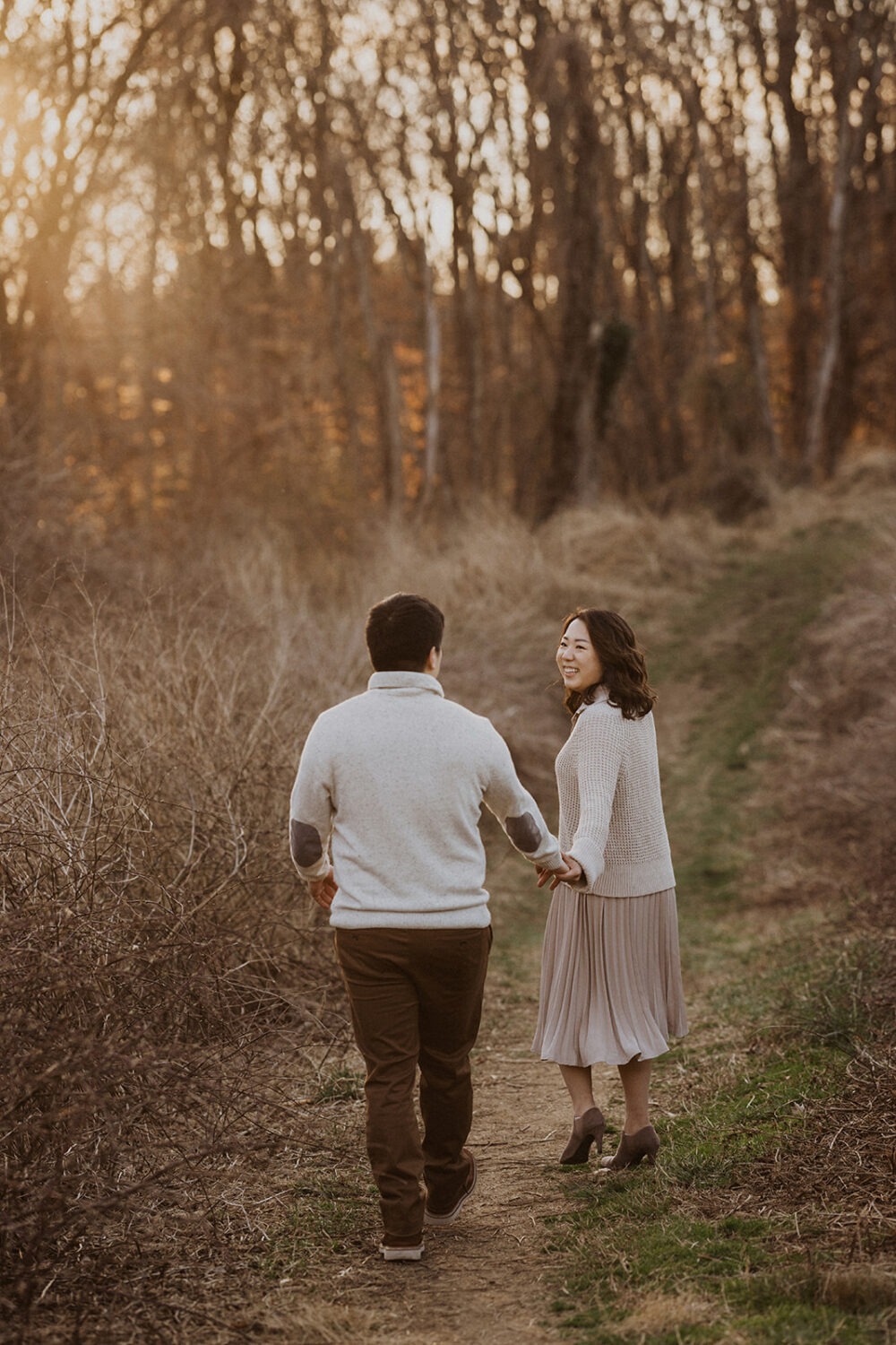 couple hold hands walking along grassy path at Rock Creek Park