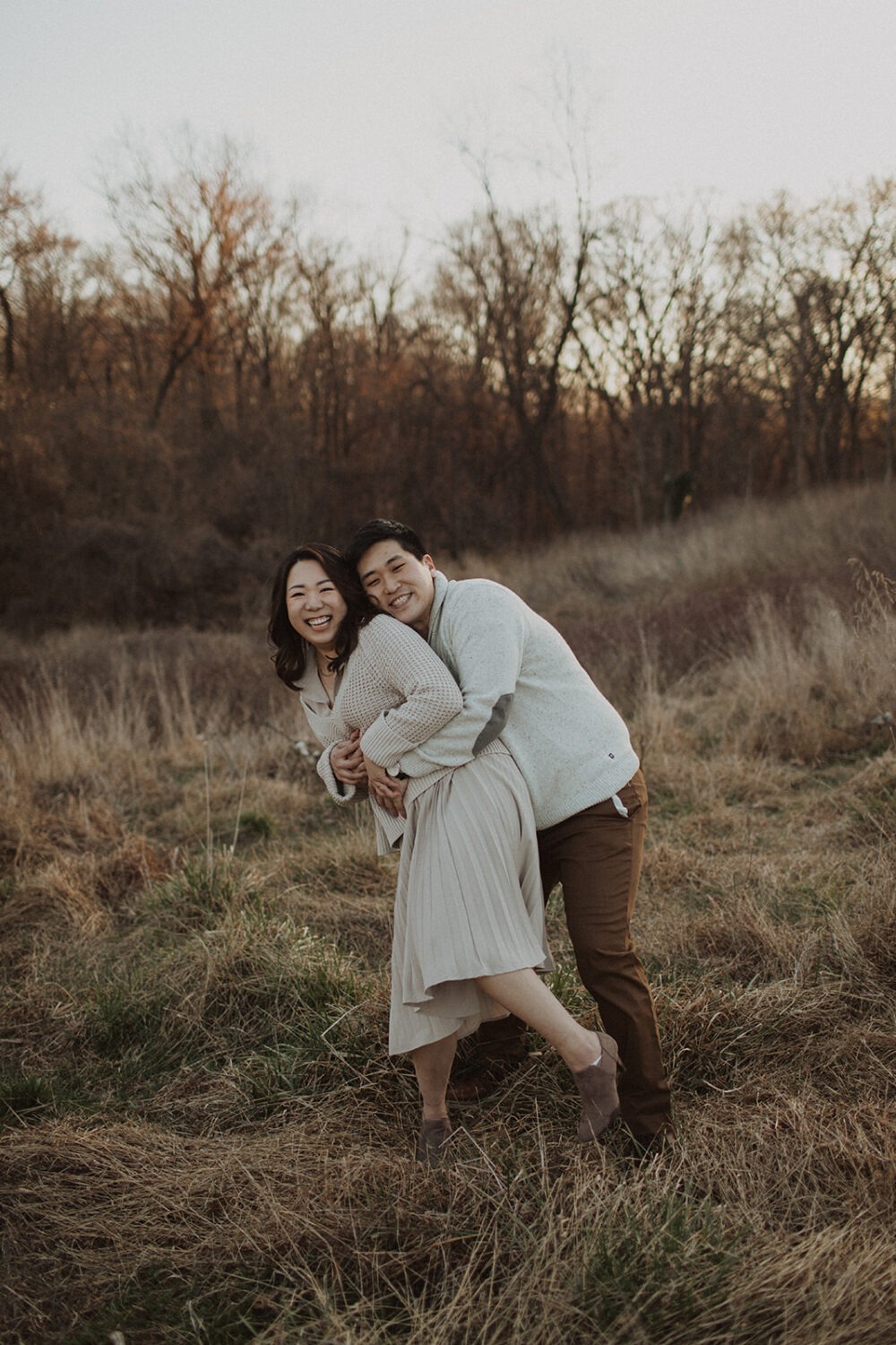 couple embrace in a grassy field taking winter engagement photos