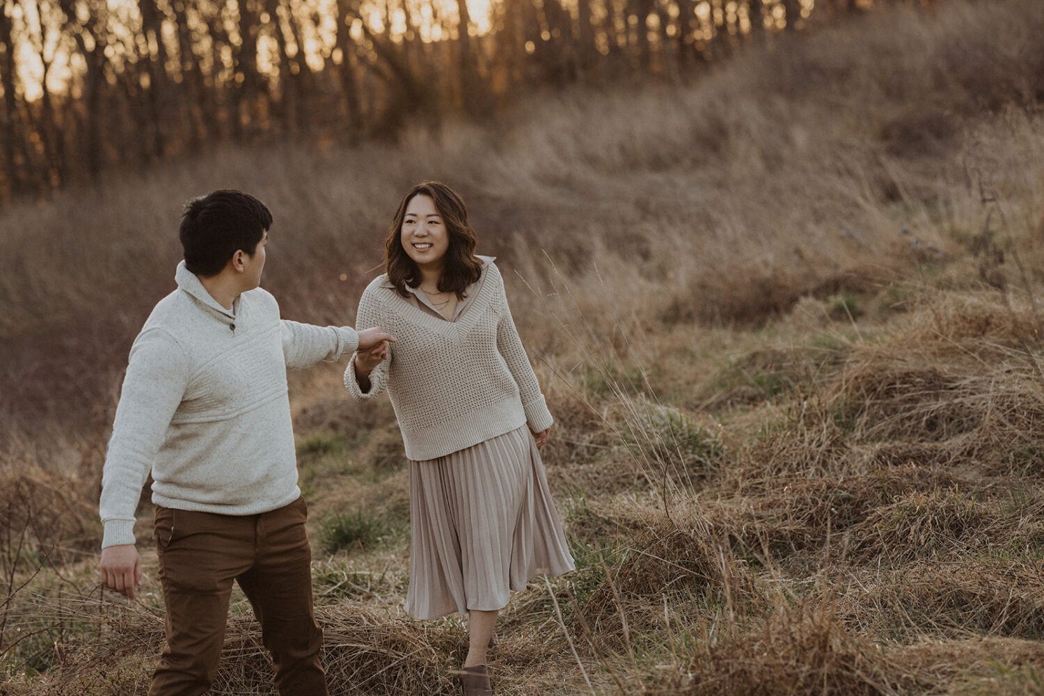 couple hold hands walking along grassy path