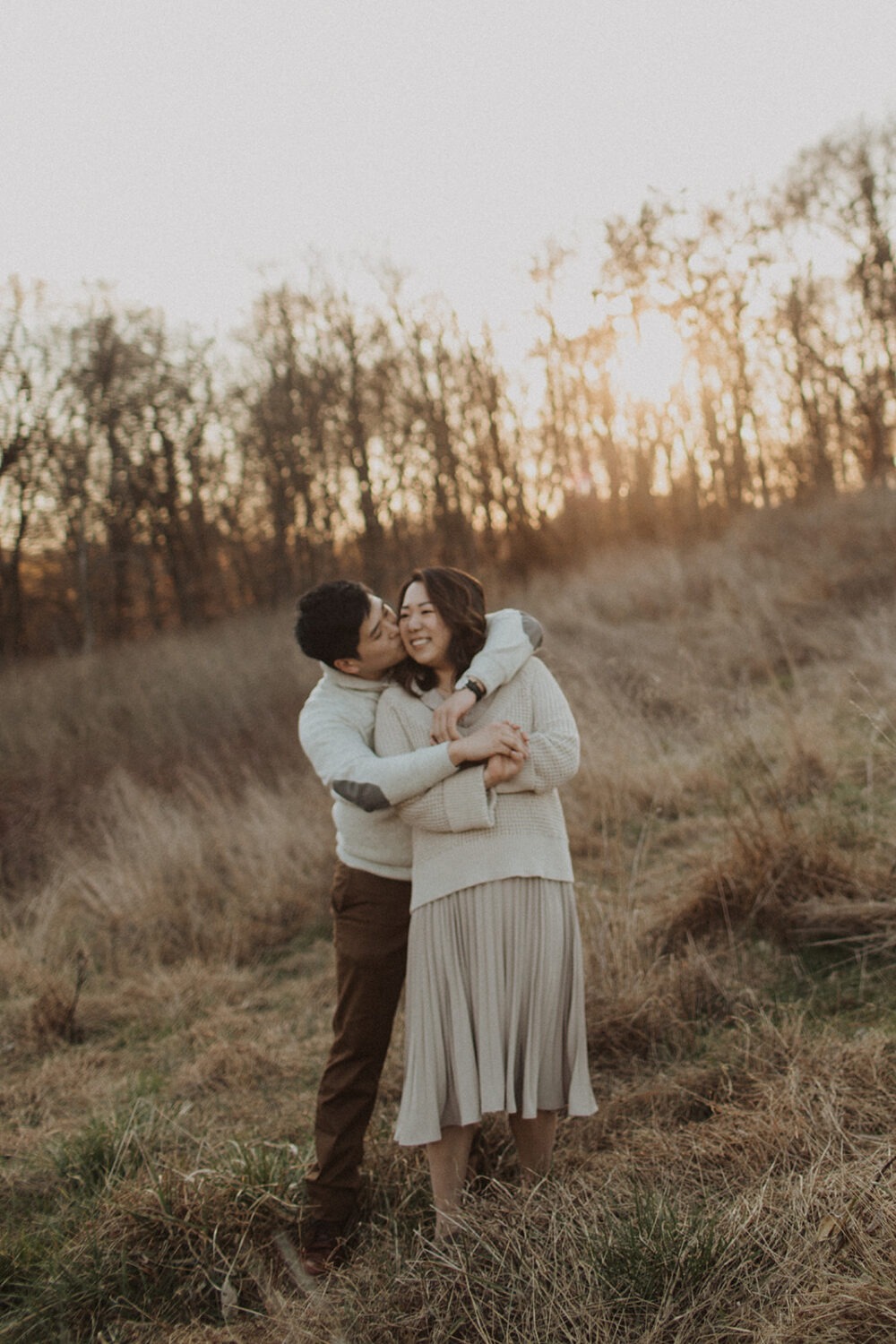 couple embrace while taking winter engagement photos in a grassy field at Rock Creek Park at sunset