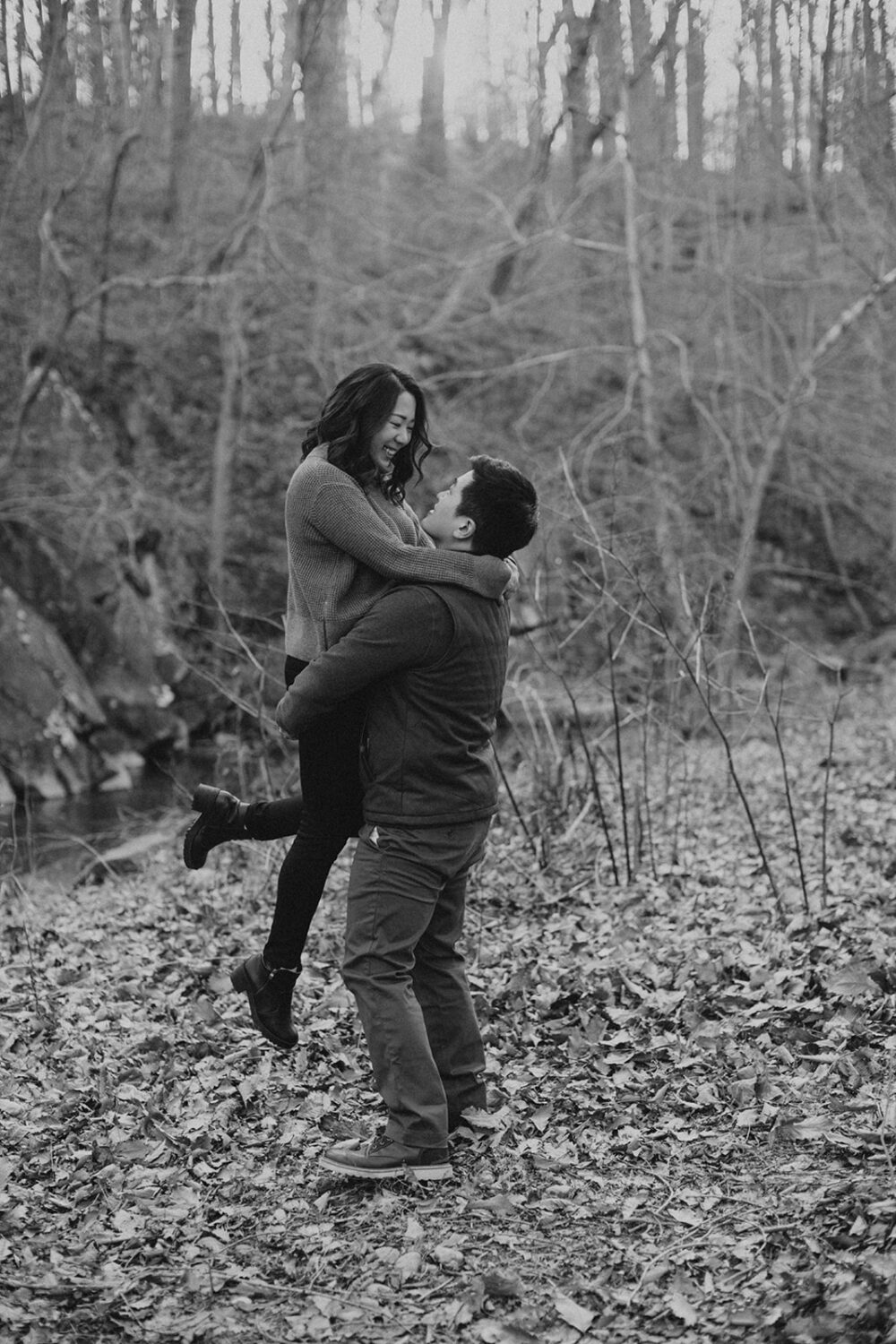 couple embrace while taking winter engagement photos by the creek