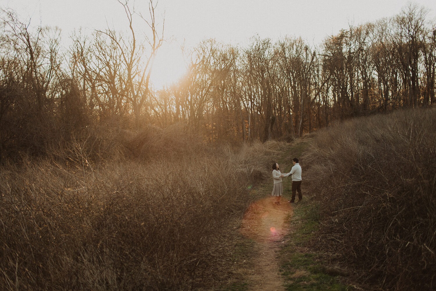 couple hold hands walking along grassy path