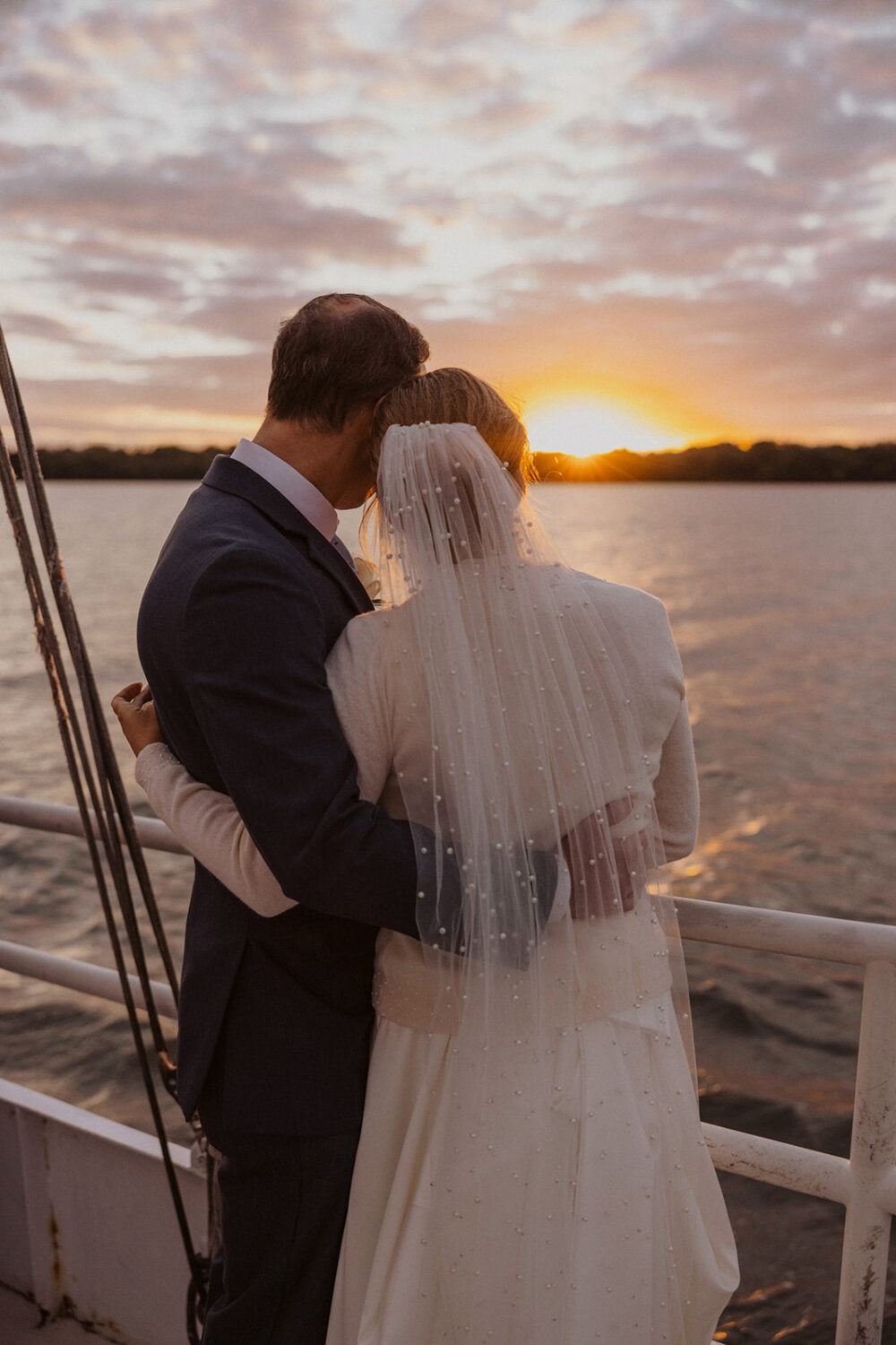couple embrace overlooking the water during sunset boat wedding