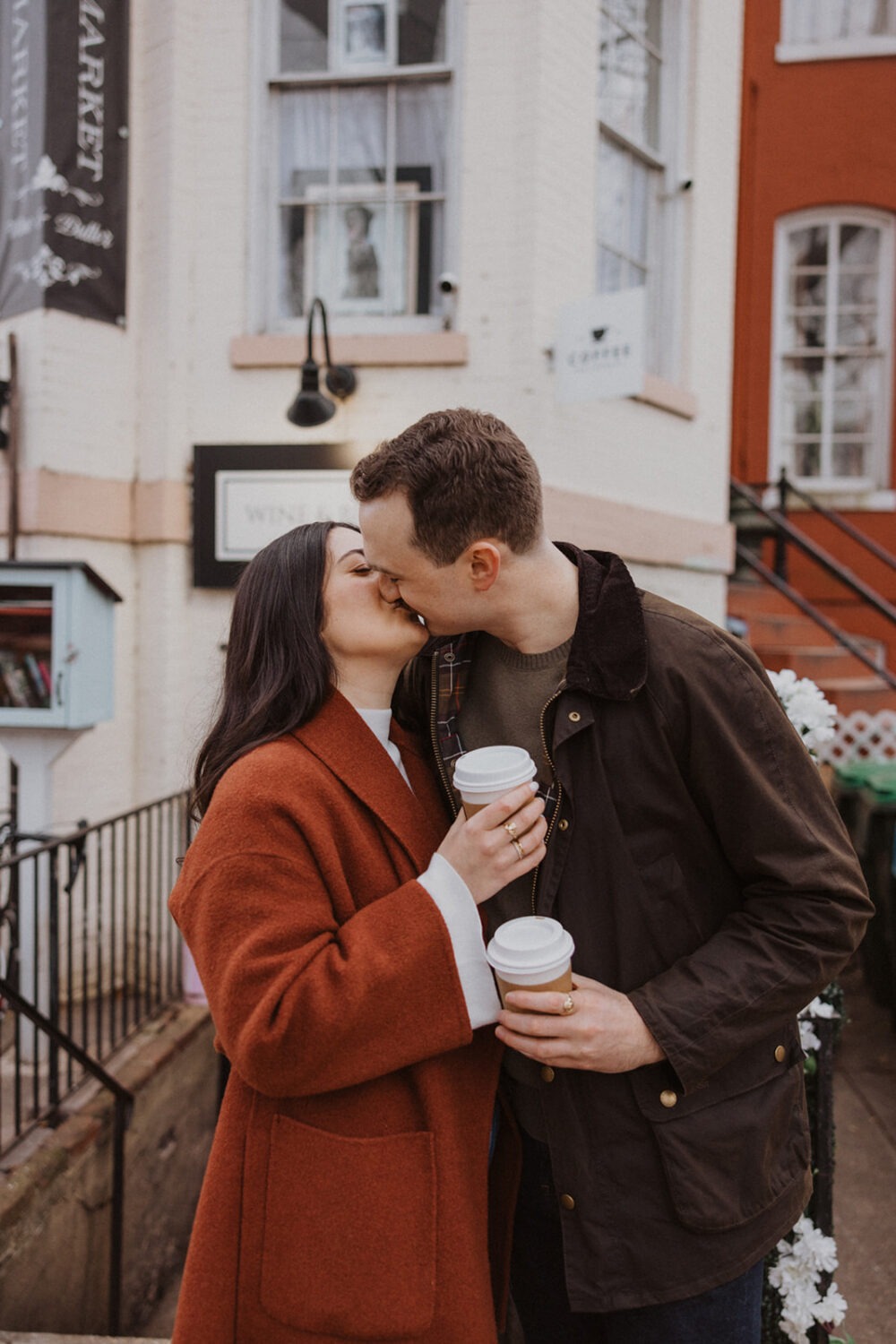 couple kiss outside coffee shop with coffee in hand