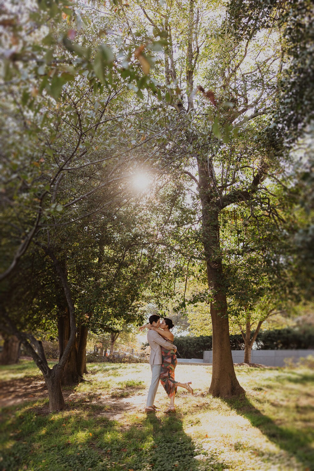 couple embrace between the trees during sunset