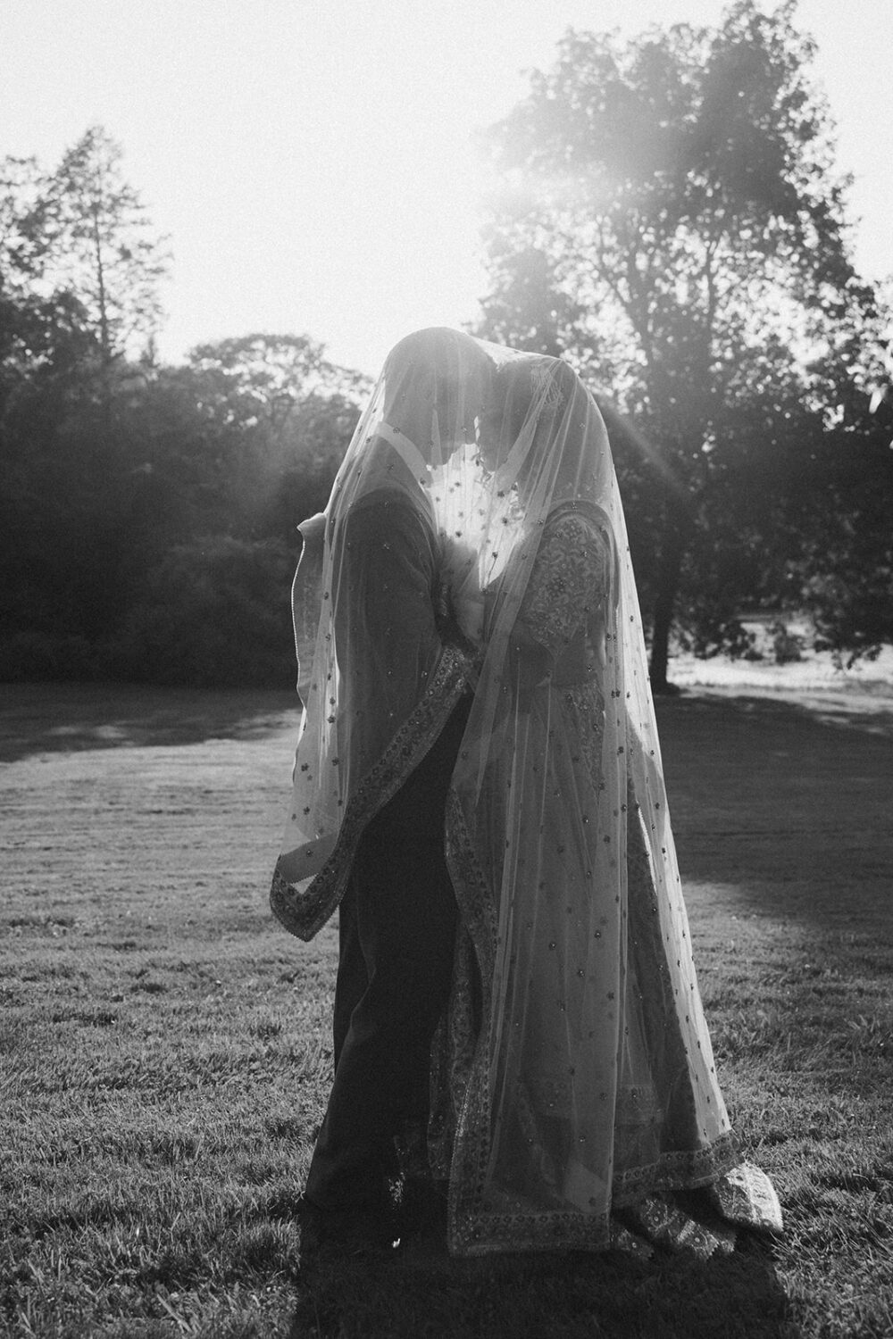 couple pose under bride's veil at sunset