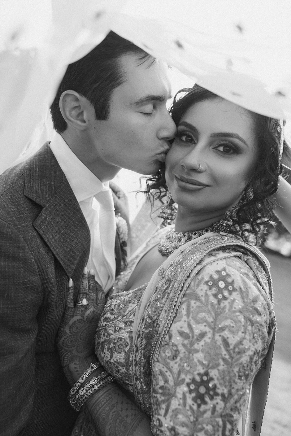 couple embrace while groom kisses bride's forehead underneath veil 