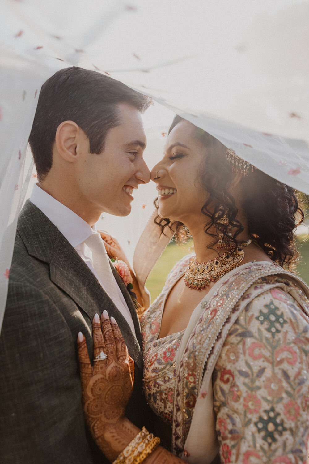 couple embrace and smile at each other under veil during sunset photos