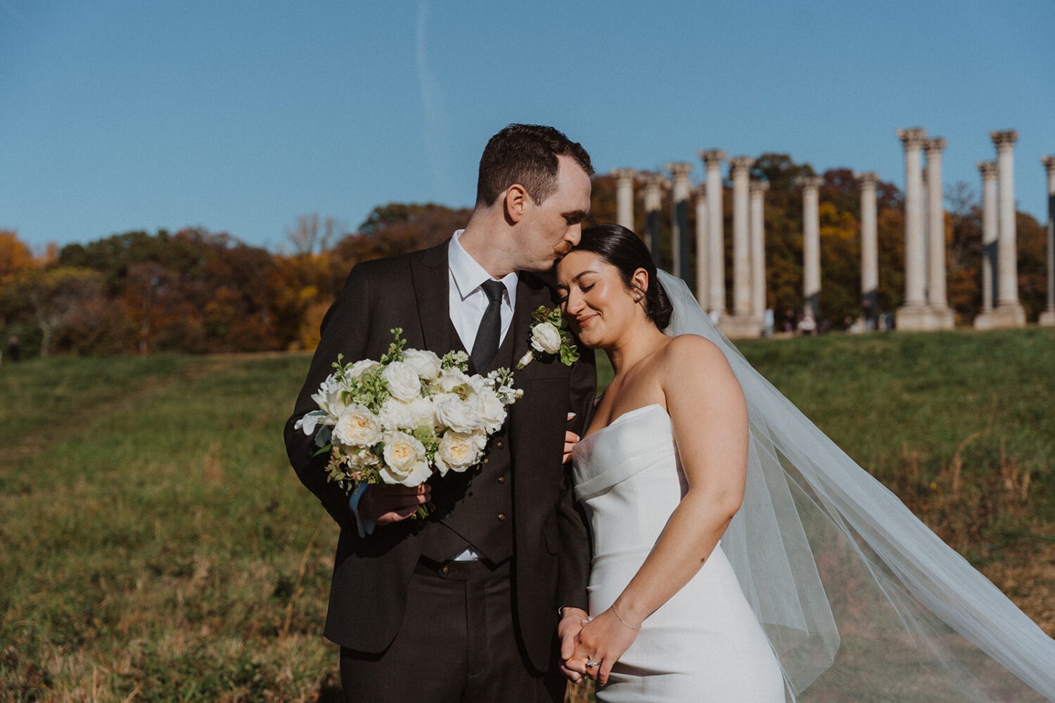 couple poses in front of National Arboretum columns on wedding day
