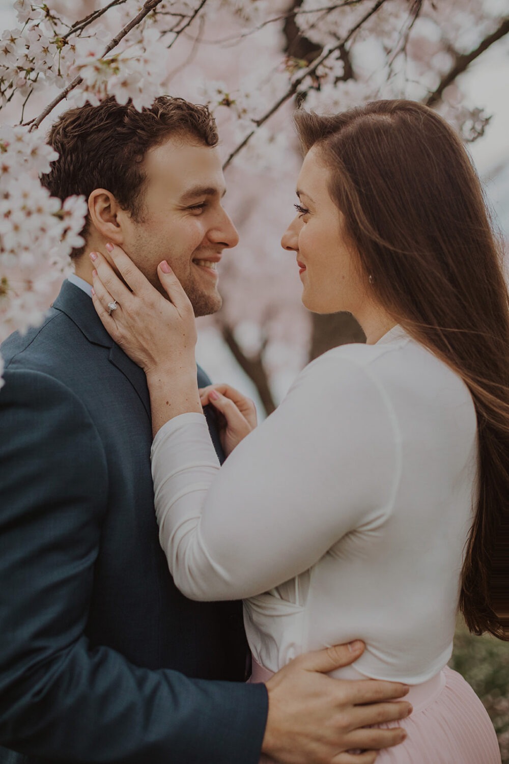 couple embrace while being surrounded by cherry blossom trees