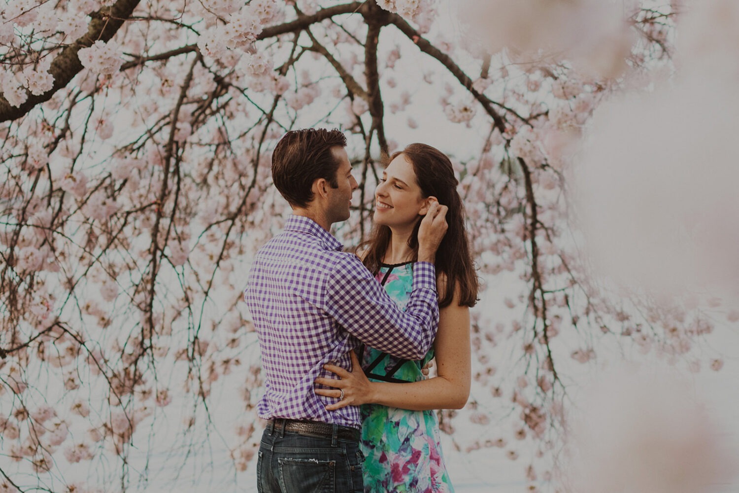 couple pose while being surrounded by cherry blossom trees