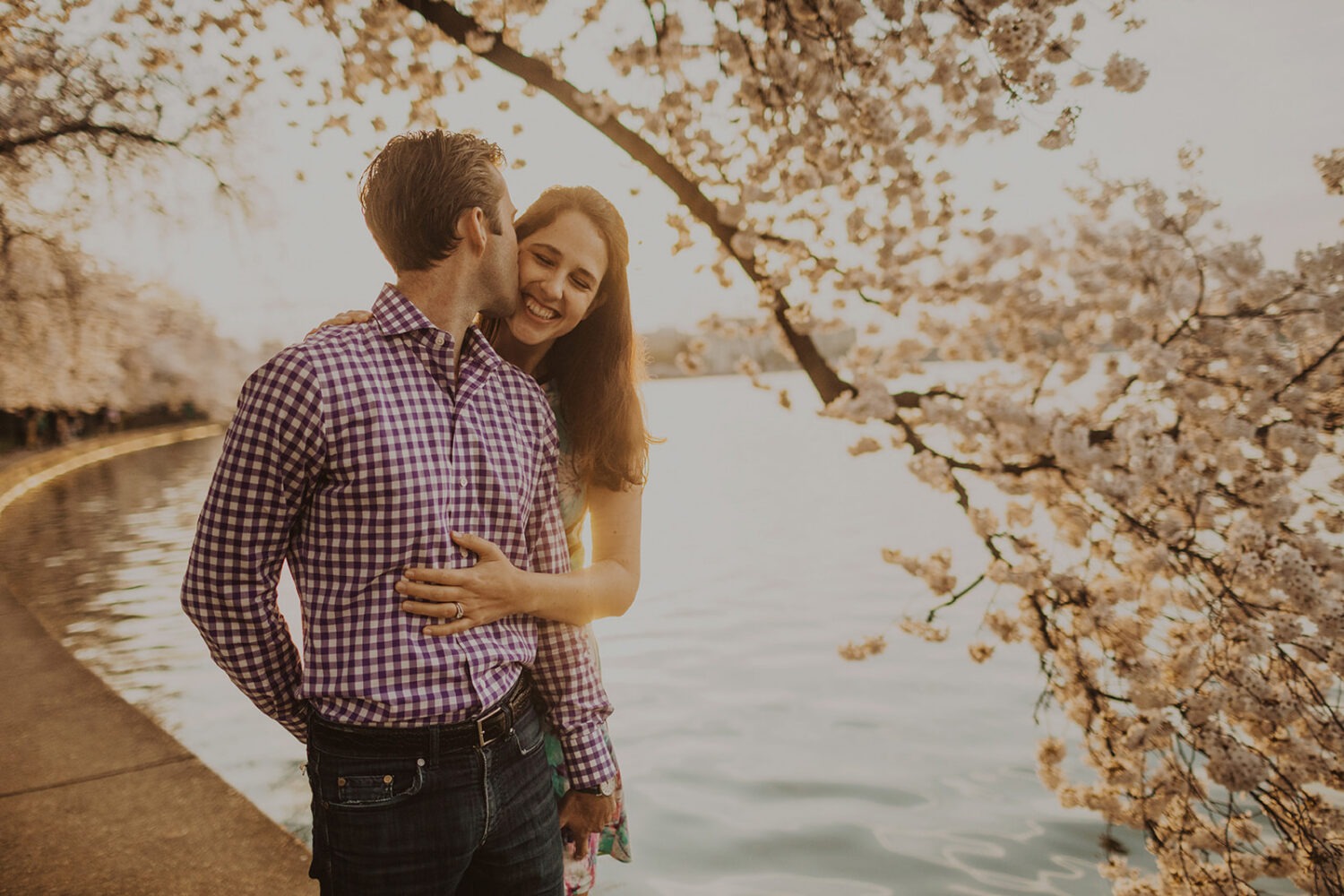 couple embrace along the water at sunset