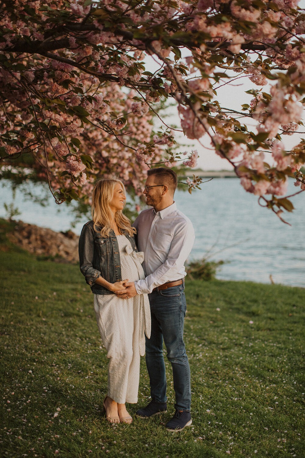 couple pose while taking maternity photos in the middle of cherry blossom trees