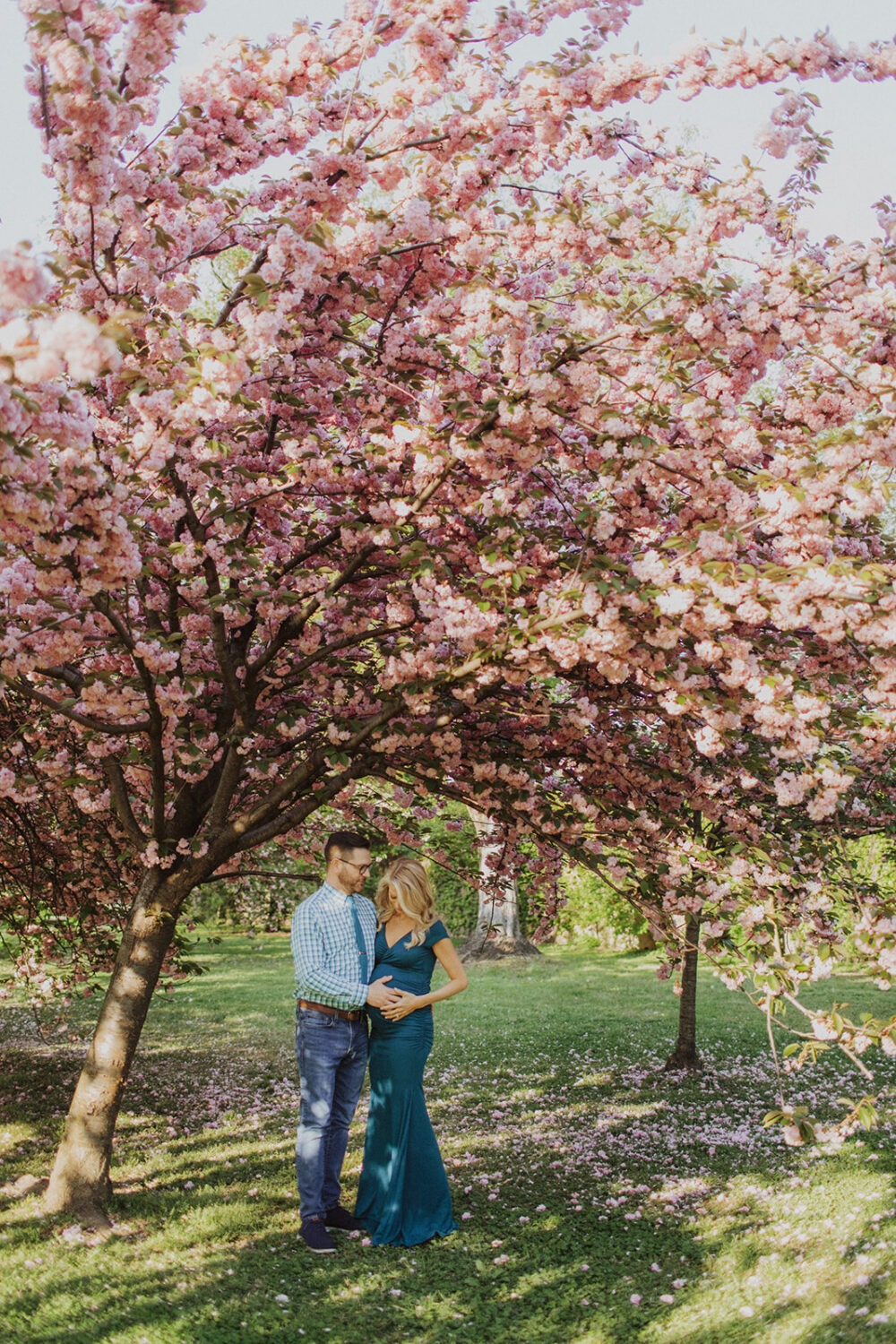 couple posing for maternity photos surrounded by cherry blossom trees