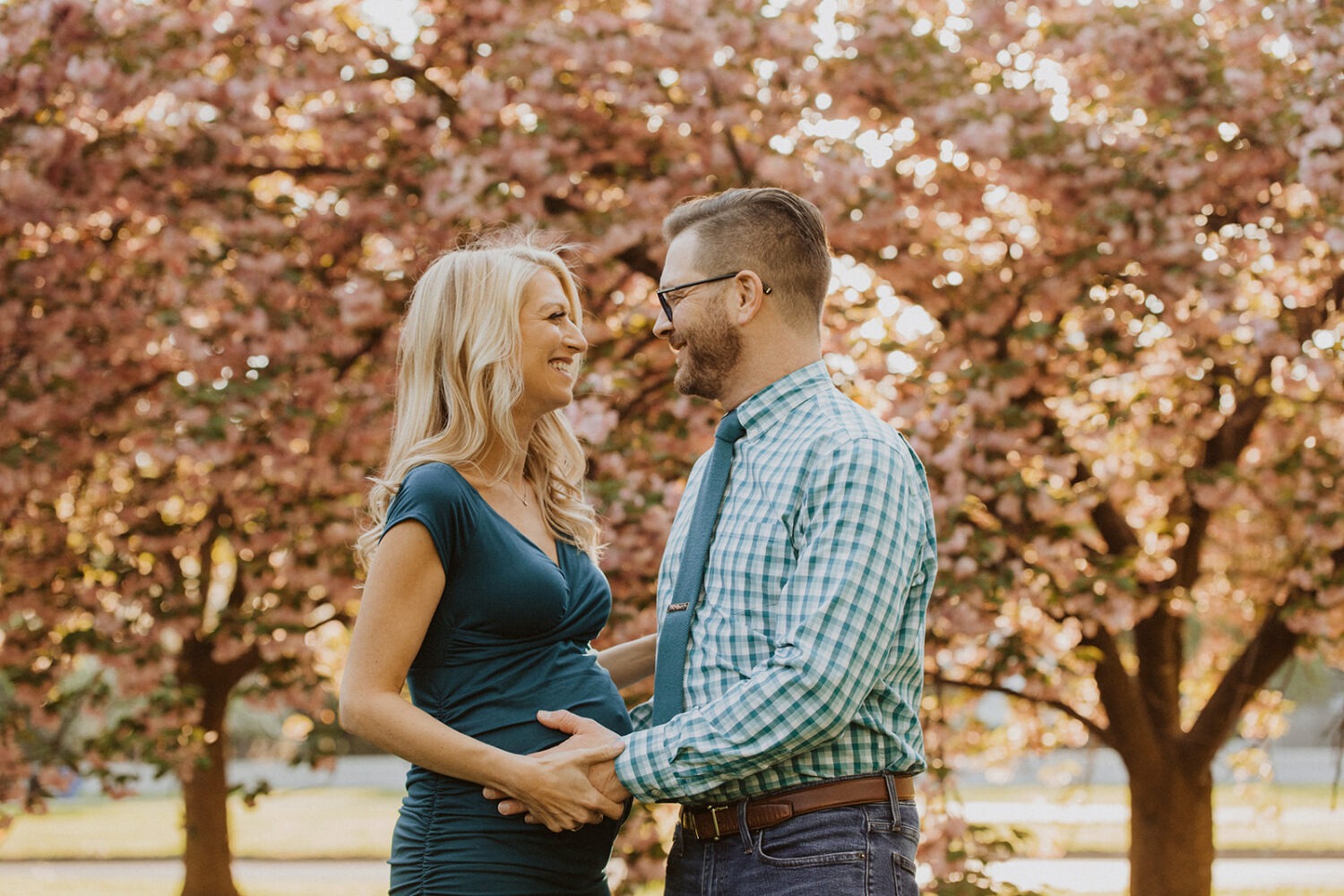 couple pose while taking maternity photos in the middle of cherry blossom trees