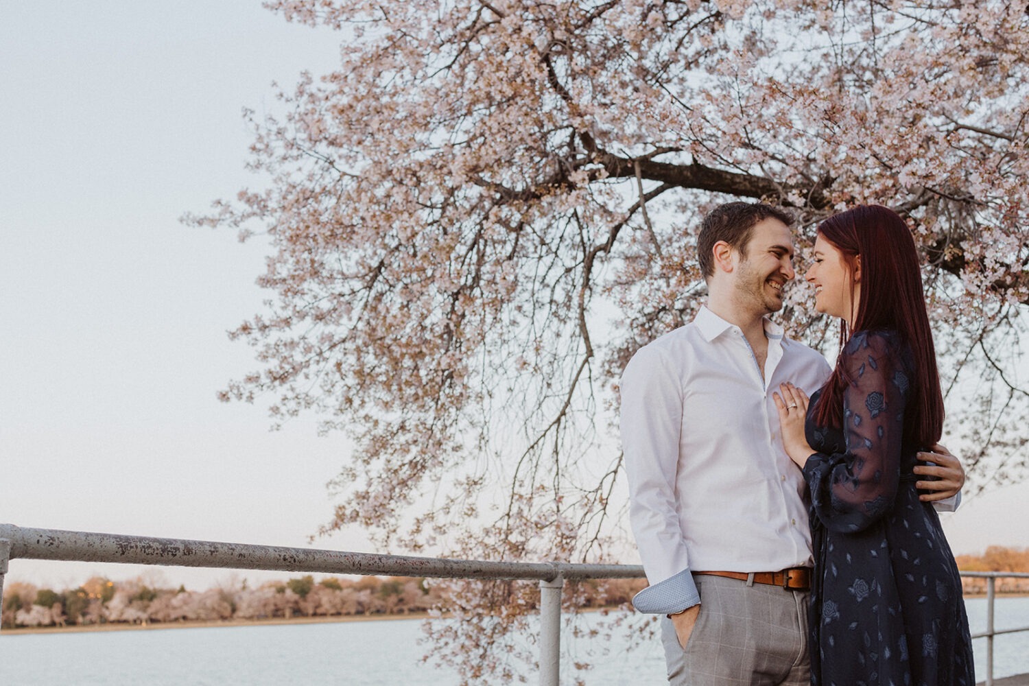 couple embrace along the water while taking DC cherry blossom photos