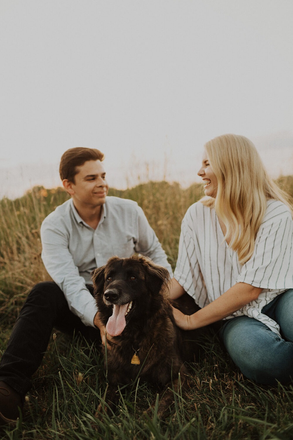 couple pose with their dog in a grassy field