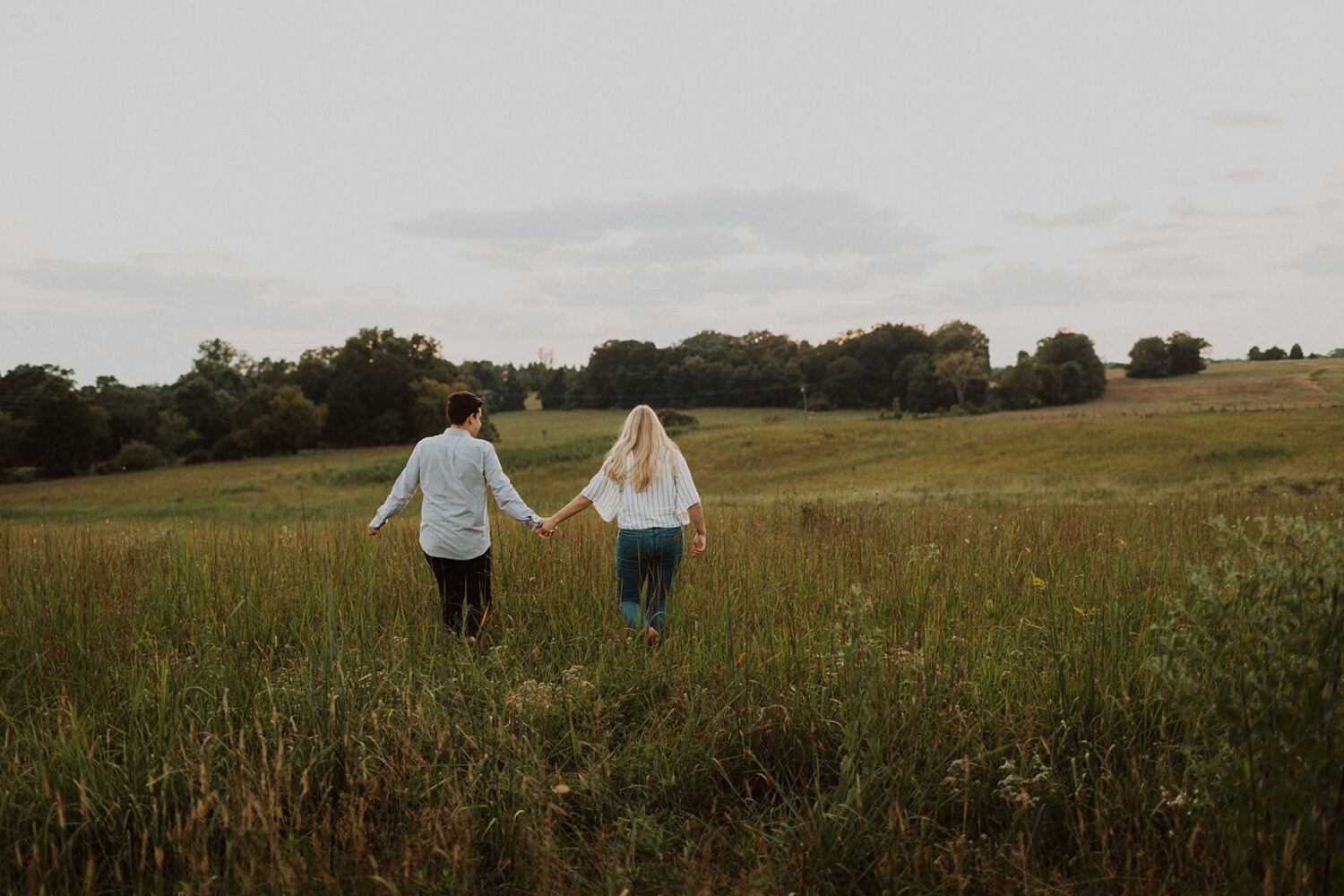 couple holding hands walking through grassy field