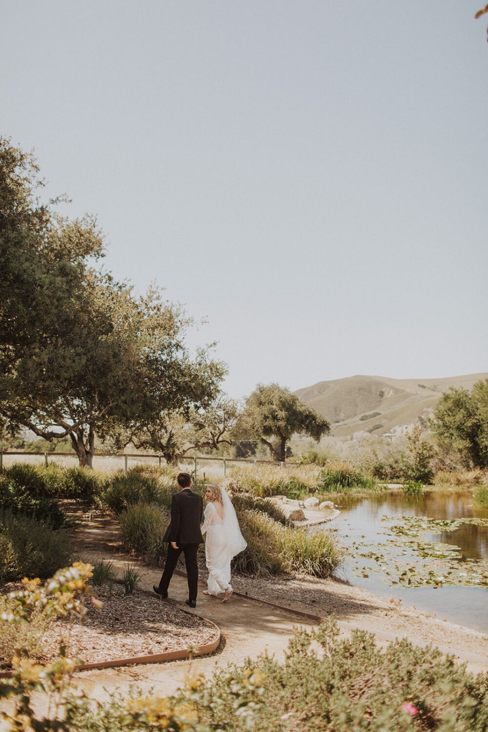 couple walk holding hands in front of lake at Alisal Ranch spring wedding