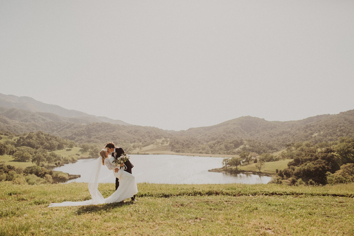 couple kiss in front of lake at Alisal Ranch spring wedding