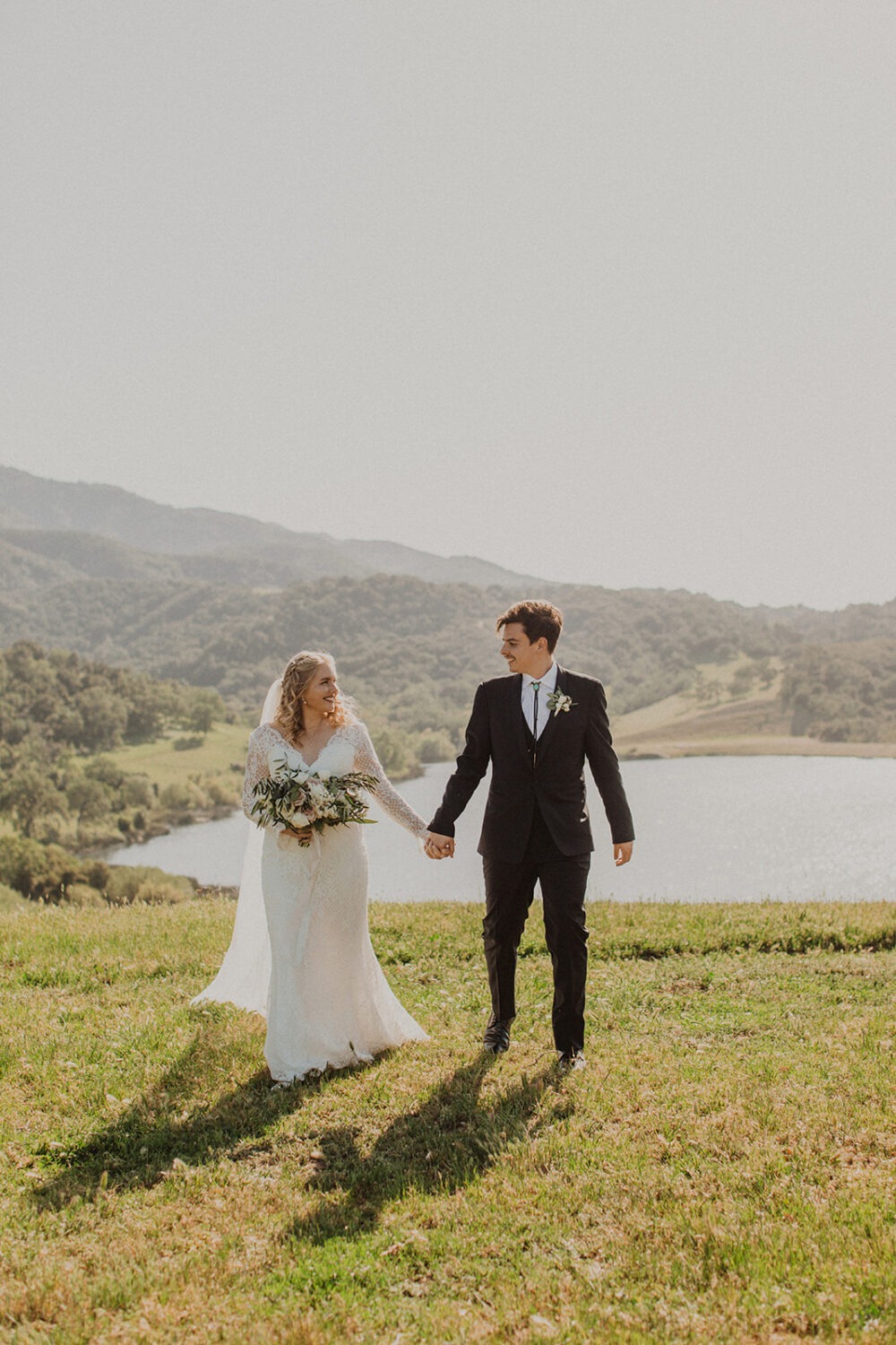 couple walk holding hands in front of lake at Alisal Ranch spring wedding