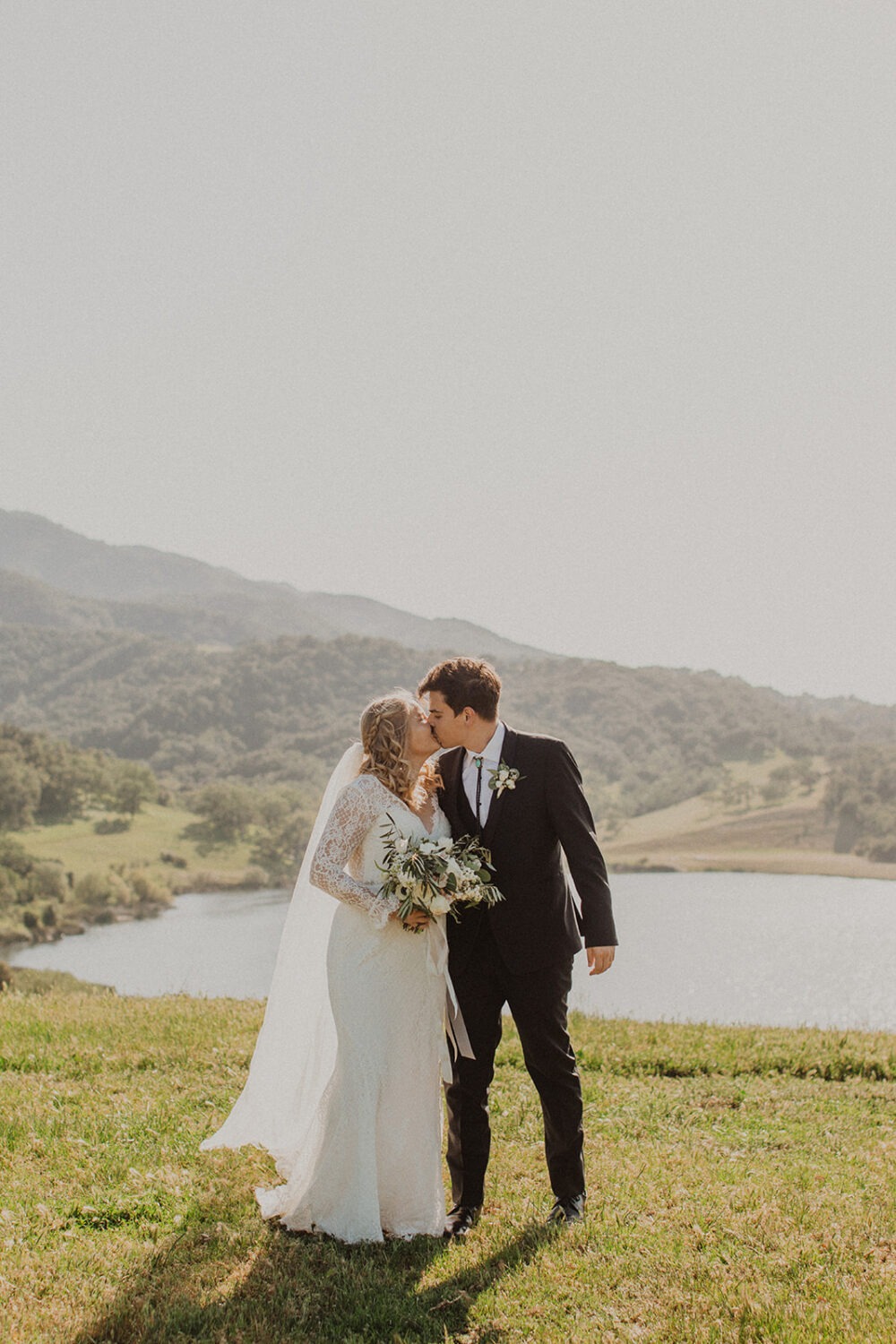couple kiss in front of lake at Alisal Ranch spring wedding