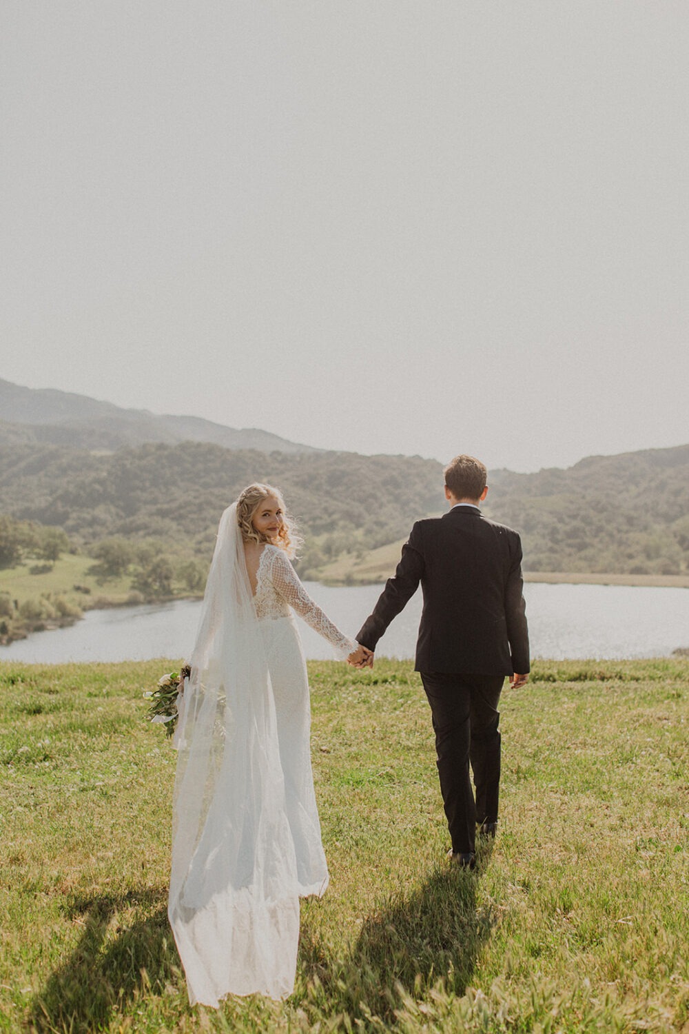 couple walk holding hands in front of lake at Alisal Ranch spring wedding