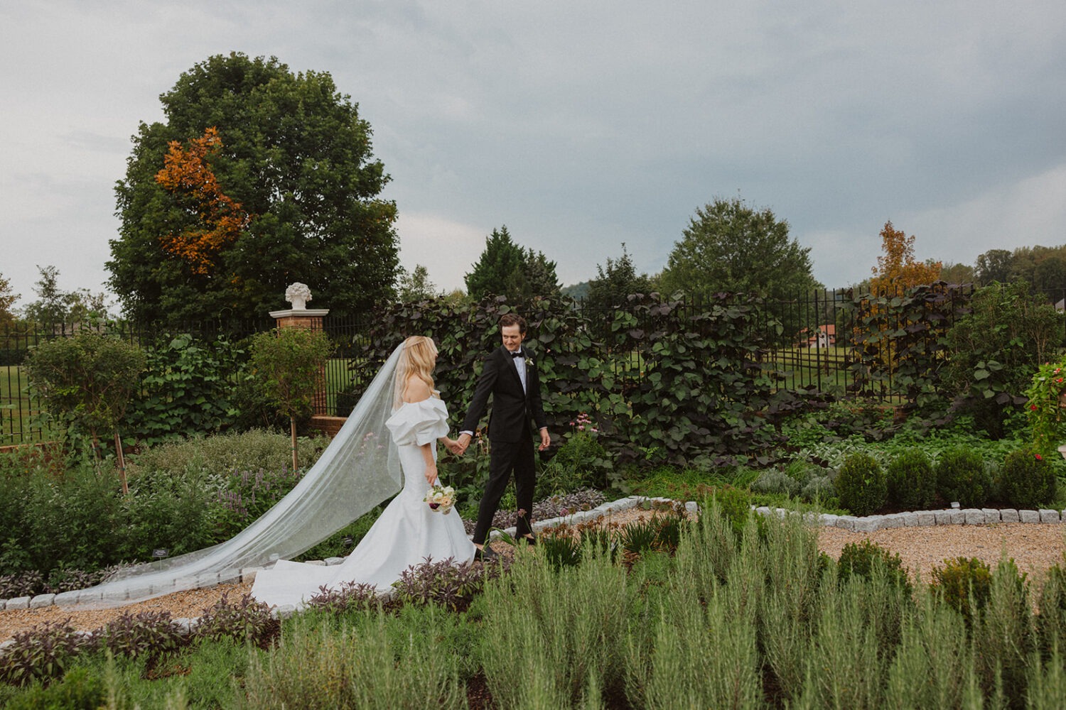 couple walking holding hands along path of greenery