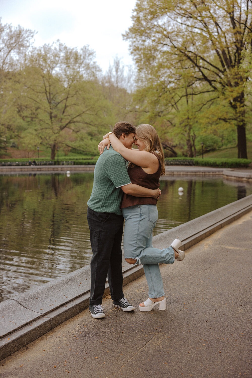 couple embrace in front of the water at Central Park while taking rainy engagement photos