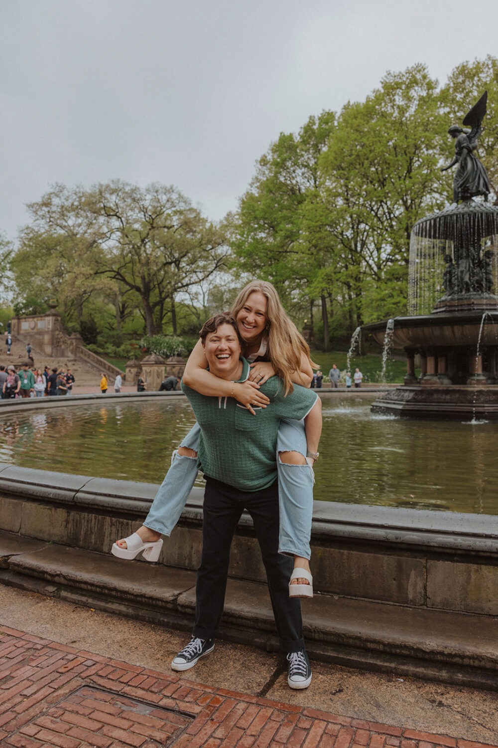 couple pose doing a piggyback ride in front of the Bethesda Fountain in NYC