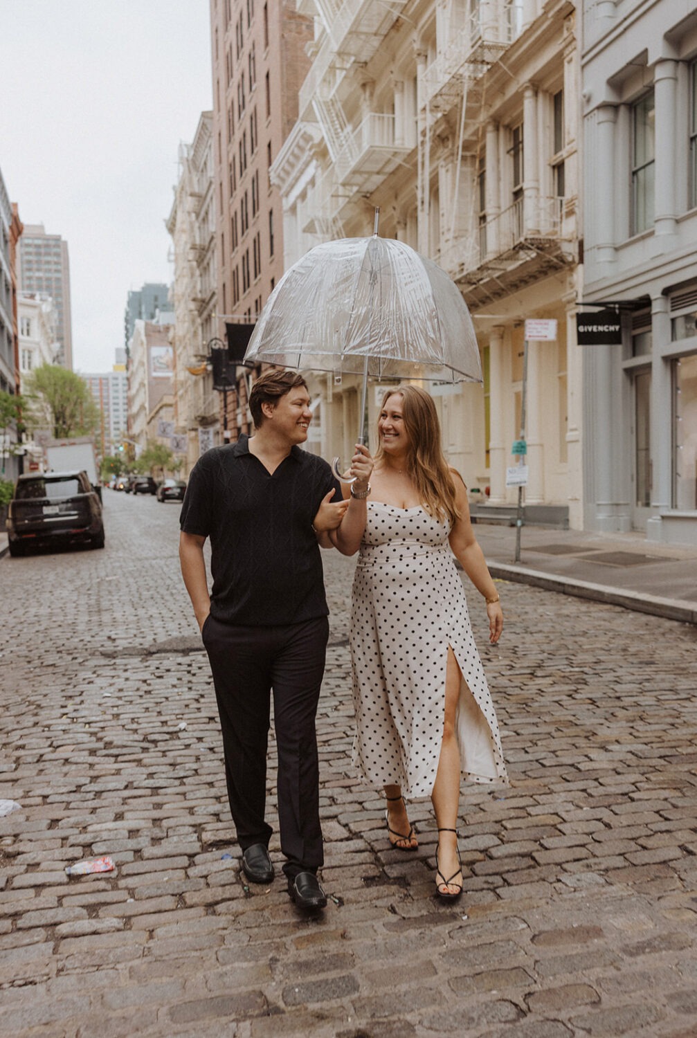 couple walking together with clear umbrellas in the middle of the street in NYC capturing rainy engagement photos