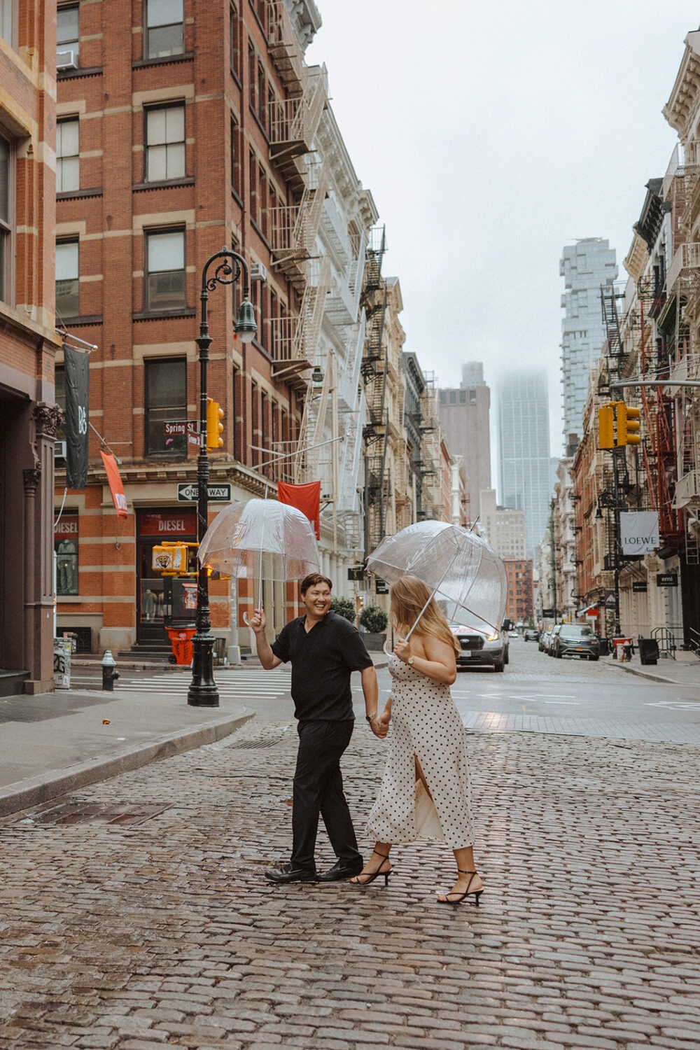 couple walking together with clear umbrellas in the middle of the street in NYC capturing rainy engagement photos