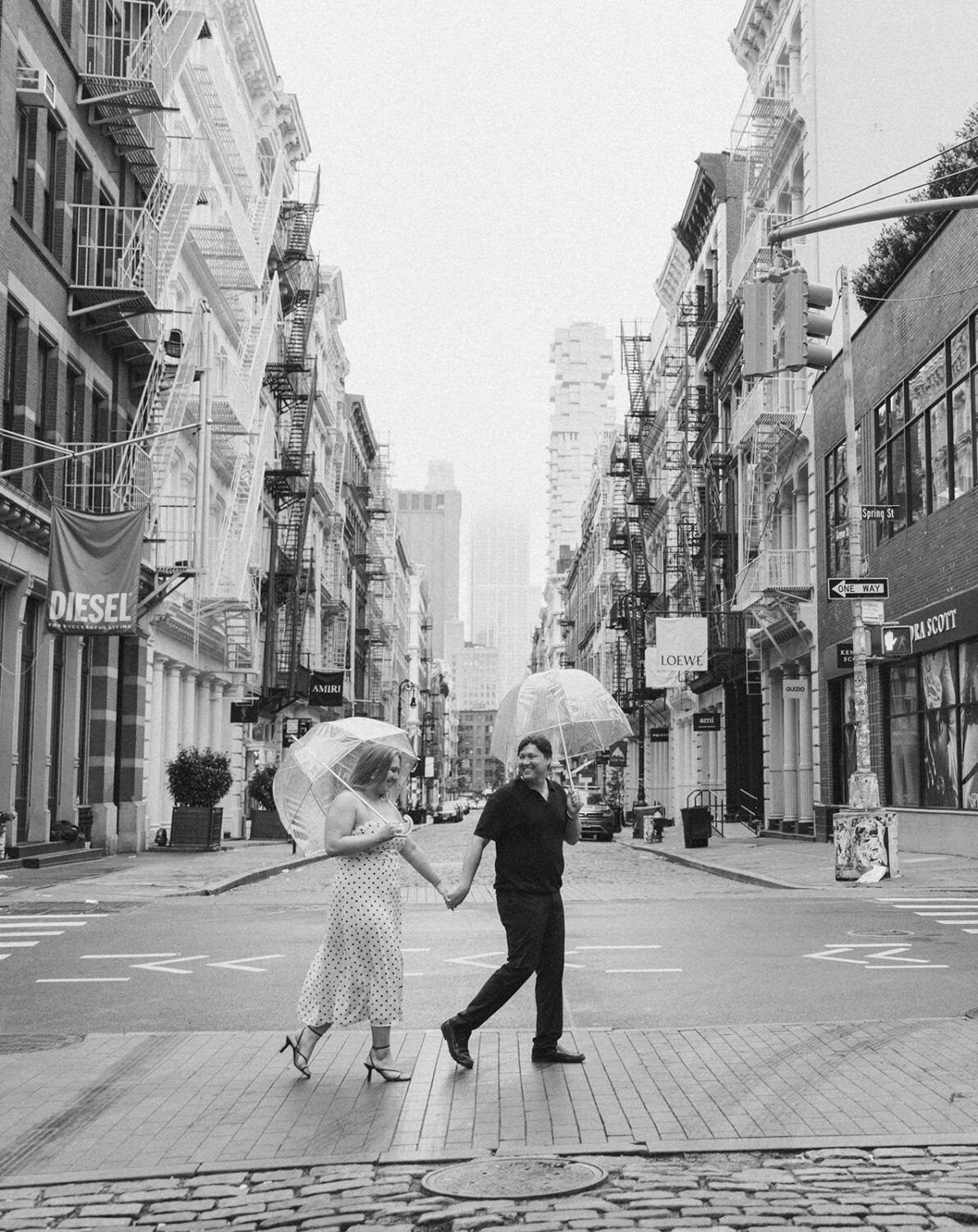 couple walking together with clear umbrellas in the middle of the street in NYC capturing rainy engagement photos