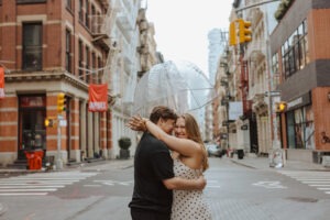 couple embrace under clear umbrella in the middle of the street in NYC capturing rainy engagement photos