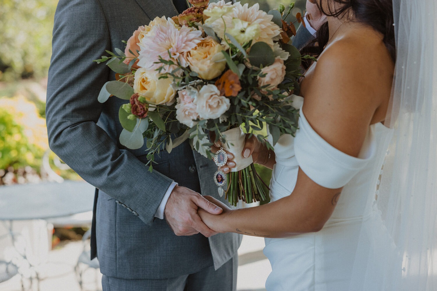 detail shot of the couple holding hands while holding wedding bouquet and photos of mother