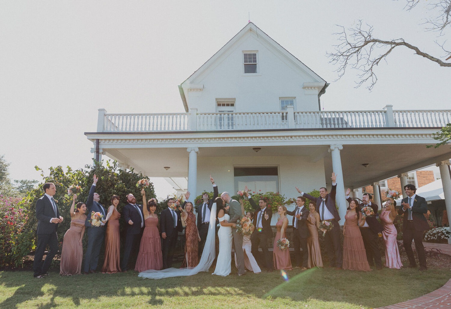 couple and wedding party pose in front of white building at River Farm Alexandria Virginia